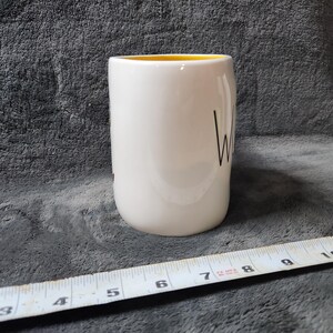 Puede incluir: Una taza de cer&aacute;mica blanca con interior amarillo. La palabra "Wine" est&aacute; escrita en escritura negra en el lateral. Una cinta m&eacute;trica est&aacute; en primer plano.