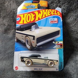 May include: A Hot Wheels die-cast toy car in a package. The car is beige and black with gold-colored wheels. The packaging features the Hot Wheels logo, the text "NEW FOR 2024", and the words "SMALL BLOC".