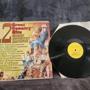 Op de afbeelding: Een vinyl platenhoes met een groep countrymuziek artiesten. Het album is getiteld "12 Great Country Hits" en bevat een lijst met artiesten waaronder Webb Pierce, Ferlin Husky, Patsy Cline, George Jones, Cowboy Copas, Carl Belew, Hank Locklin, Jimmy Dean, Justin Tubb, T. Texas Tyler, Red Sovine en Slim Willet. Het album is een uitgave van Hilltop Records.