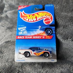 May include: A blue and white Hot Wheels '57 Chevy die-cast car in its original packaging. The packaging is blue with the Hot Wheels logo and text that reads "Race Team Series II". The car has the text "Blown Engine!"