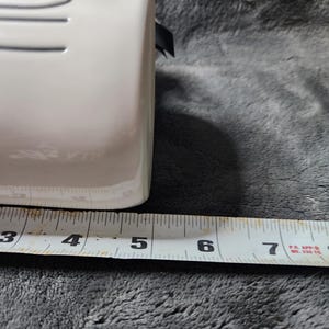 K&ouml;nnte beinhalten: Ein wei&szlig;er rechteckiger Keramikbeh&auml;lter mit einem schwarzen Band. Der Beh&auml;lter wird mit einem Ma&szlig;band gemessen, das eine Breite von etwa 10 cm zeigt.