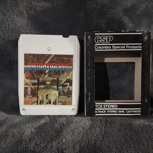 Può includere: Una cartuccia per nastro stereo a 8 tracce e la sua custodia in cartone nero. Il nastro è bianco con un'etichetta colorata con testo e un'illustrazione di un gazebo. La custodia è nera con testo bianco, tra cui "Columbia Special Products".