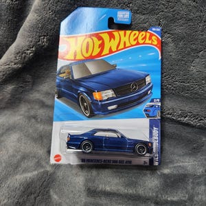 May include: A blue Hot Wheels die-cast model of a '89 Mercedes-Benz 500 SEC AMG. The car is displayed on a blue and white card with the Hot Wheels logo and the text "GUARANTEED FOR LIFE". The model is 1/64 scale.