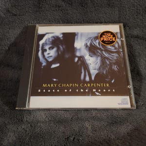 May include: A CD case for Mary Chapin Carpenter's album, "State of the Heart." The cover shows a black and white image of the artist. The disc case has a "The Nice Price" sticker.