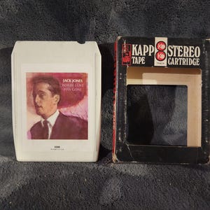May include: Vintage 8-track tape cartridge of Jack Jones' album "Where Love Has Gone." The white cartridge features a portrait of Jones. The cardboard sleeve is black and red, with "KAPP TAPE STEREO CARTRIDGE" printed on it.