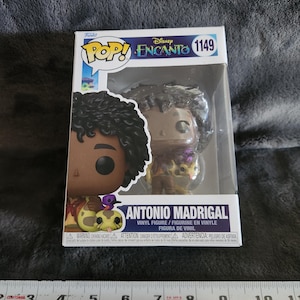 Puede incluir: Figura de vinilo Funko Pop! de Antonio Madrigal de Disney's Encanto, en una caja transparente. La figura tiene cabello rizado oscuro y viste un atuendo detallado. La caja presenta los logotipos de Funko Pop! y Disney Encanto.