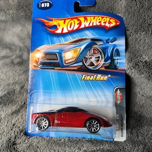May include: A red Hot Wheels die-cast car on a blue and orange card. The car is a Final Run Buick Wildcat model. The card features the Hot Wheels logo and the number 073. The car is red with black accents and silver wheels.