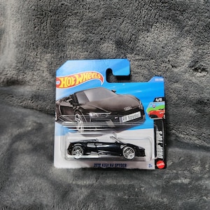 Puede incluir: Un coche de juguete negro Audi R8 Spyder 2019 en una tarjeta Hot Wheels azul y blanca. La tarjeta presenta una imagen del coche y el texto "DROP TOPS". El coche es 4/5 de la serie.