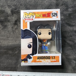 May include: A Funko Pop! Animation figure of Android 17 from Dragon Ball Z. The figure is in a box with the Pop! Animation logo. The figure is wearing a black shirt, orange vest, blue pants, and black boots. The box is approximately 4 inches wide.