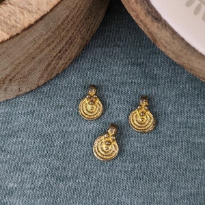 Op de afbeelding: Een houten doos met een deksel, gevuld met kleine gouden metalen bedels. Het deksel heeft een decoratief ontwerp. Drie bedels worden getoond op een blauwe stoffen ondergrond.