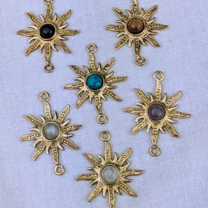 Könnte beinhalten: Sechs goldene Sonnen-Anhänger mit verschiedenen Edelsteinen in der Mitte. Die Anhänger haben zwei Ösen zum Anbringen an Schmuck.