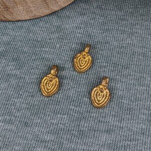 May include: A wooden box with a lid, filled with small gold-colored metal charms. The lid has a white background with a gray mandala design. Three of the charms are sitting on a gray surface.