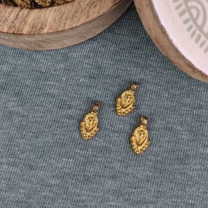 以下が含まれることがあります： 蓋付きの木箱の中に、涙の形をした小さな金色の金属製のチャームがたくさん入っています。チャームのうちの3つは箱の外に置かれています。