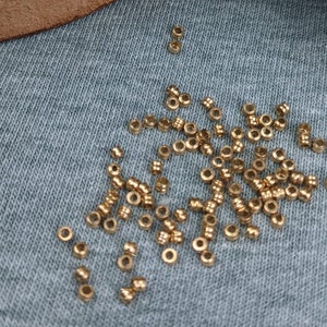 Könnte beinhalten: Eine Holzkiste gefüllt mit kleinen, goldfarbenen Metallperlen. Die Kiste ist geöffnet und einige Perlen sind auf einer blauen Stoffoberfläche verstreut.
