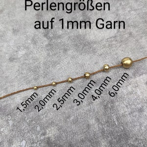 May include: A close-up of a string of gold beads of varying sizes, ranging from 1.5 mm to 6.0 mm, strung on a brown thread. The text "Perlengr&ouml;&szlig;en auf 1 mm Garn" is visible above the beads.