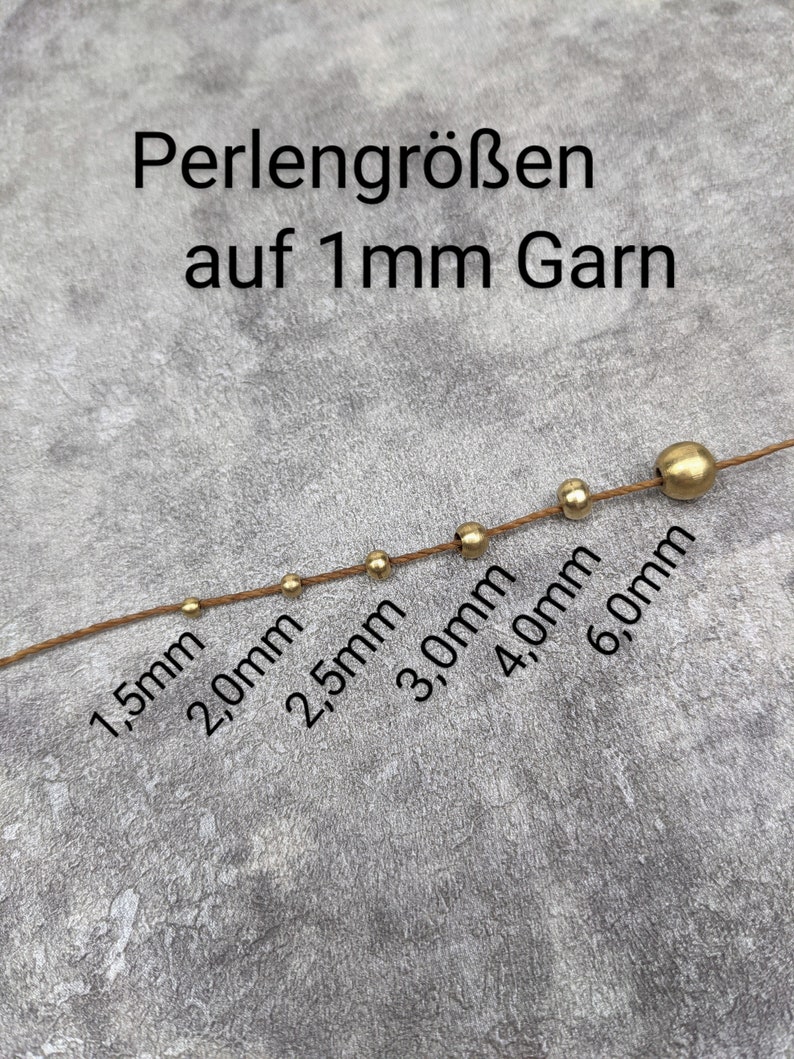 May include: A close-up of a string of gold beads of varying sizes, ranging from 1.5 mm to 6.0 mm, strung on a brown thread. The text "Perlengr&ouml;&szlig;en auf 1 mm Garn" is visible above the beads.