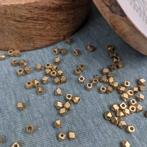 Op de afbeelding: Een houten kom gevuld met goudkleurige metalen kralen. De kralen zijn verspreid over een blauw stoffen oppervlak.