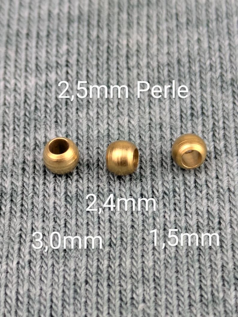 May include: Three gold-colored metal beads of different sizes. The beads are 2.5mm, 2.4mm, and 1.5mm in diameter. The beads are on a gray textured surface.