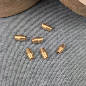 May include: Six gold-coloured metal beads, each with a cylindrical shape, are scattered on a blue fabric surface.