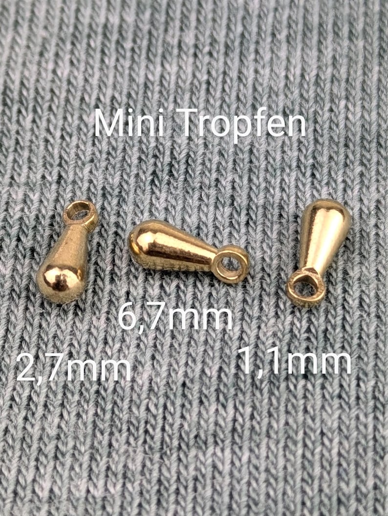 Pode incluir: Tr&ecirc;s pingentes de metal em forma de l&aacute;grima de cor dourada com um la&ccedil;o no topo. Os pingentes medem 2,7 mm, 6,7 mm e 11 mm. O texto "Mini Tropfen" &eacute; vis&iacute;vel acima dos pingentes.