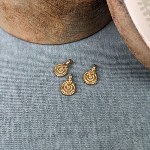 Op de afbeelding: Drie goudkleurige metalen bedels met een cirkelvormig ontwerp. De bedels hebben een verhoogd, concentrisch cirkelpatroon.