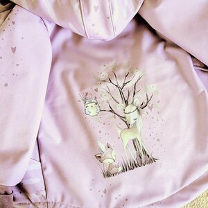 Könnte beinhalten: Helllila Jacke mit Kapuze und Reißverschluss. Das Innenfutter zeigt eine skurrile Illustration von Hirsch, Fuchs und Baum. Die Ärmel der Jacke haben ein Herzmuster und eine helllila Farbe.