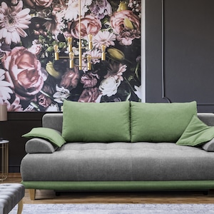 Könnte beinhalten: Ein graues und grünes Sofa mit einer floral gemusterten Wand dahinter. Das Sofa hat eine gesteppte Rückenlehne und einen grünen Besatz am unteren Rand.