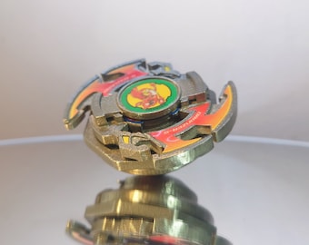 May include: A gold and red spinning top with a red and yellow dragon design. The top has a green and yellow center with a red and yellow dragon image. The top is called "Draciel S-F".