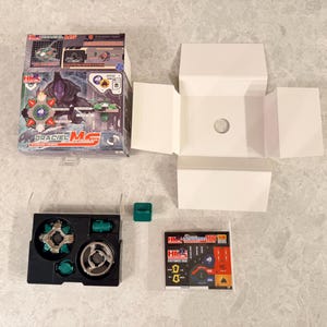 May include: An opened box set of a Draciel MS spinning top toy. The box features a graphic of the toy and its components. The set includes a black and green storage case, a green cube, and a small instruction sheet.
