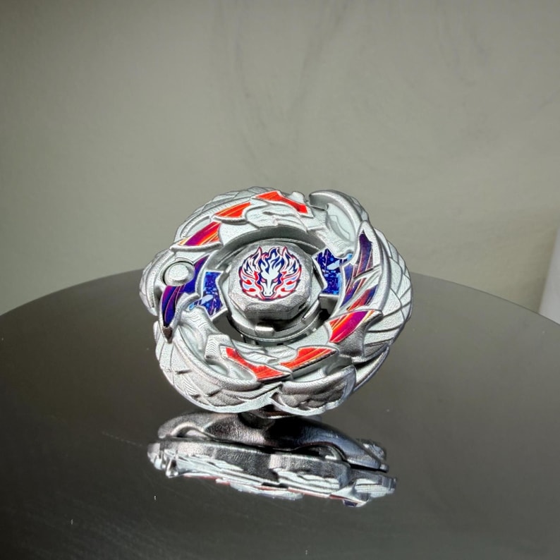 Puede incluir: Un trompo plateado y multicolor con un dise&ntilde;o detallado. La parte superior presenta detalles en rojo, azul y morado, y un emblema central. El juguete est&aacute; dise&ntilde;ado para girar y luchar.