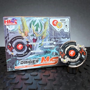以下が含まれることがあります： 箱入りのHeavy Metal System Driger MS Benchblade 2025のおもちゃ。箱には、白いと緑色の生き物のイラストが描かれています。おもちゃは黒、シルバー、赤で、「METAL SYSTEM」の文字が入っています。