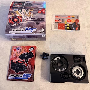 May include: A boxed toy set featuring a red and black spinning top with a detailed illustration of a tiger. The box includes the toy, a launcher, stickers, and an instruction manual. The set is labeled "Driger MF Metal Fang Standard Version".