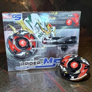 May include: A boxed toy set featuring a black, red, and gold spinning top with a matching launcher. The box has a tiger illustration and text that reads "DRIGER" and "Heavy Metal System". A second spinning top is visible.