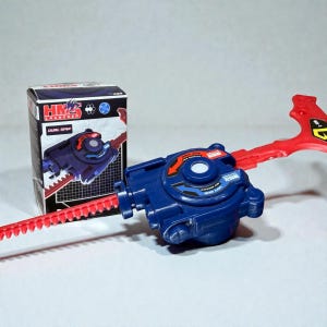 May include: A blue and red toy launcher with a box. The launcher has a red pull cord and a blue body with a circular design. The box is black and red with the text "HM2 Launcher" and a graphic of the launcher.