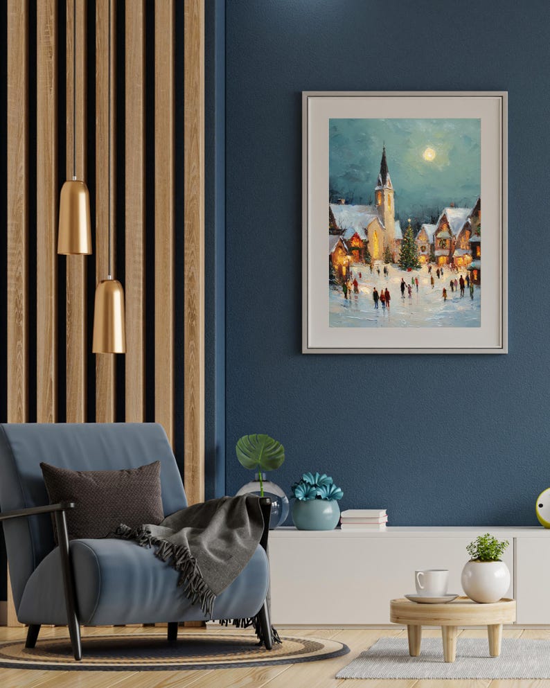 May include: A framed winter landscape painting depicts a snow-covered village with a church and a full moon. The artwork is displayed on a dark blue wall, complemented by a blue armchair, a wooden side table, and gold pendant lights.