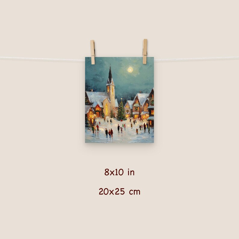 May include: An 8x10 inch print of a winter village scene. The artwork depicts a snow-covered town square with a church, houses, and a Christmas tree. People are walking in the square under a full moon. The print is held by two wooden clips.