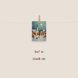 May include: A 5x7 inch print of a winter village scene, clipped to a string. The artwork depicts a snow-covered town square with a church, houses, and people. The painting has a soft, warm color palette with a full moon in the sky.
