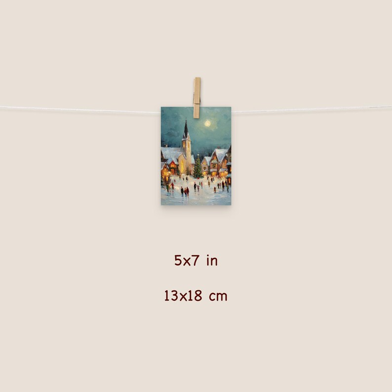 May include: A 5x7 inch print of a winter village scene, clipped to a string. The artwork depicts a snow-covered town square with a church, houses, and people. The painting has a soft, warm color palette with a full moon in the sky.