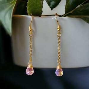 May include: A pair of gold dangle earrings with iridescent pink teardrop-shaped crystals.