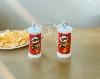 May include: A pair of earrings featuring a red and white Pringles can design with the text "Pringles Original". The earrings are made of silver and have a hook closure.