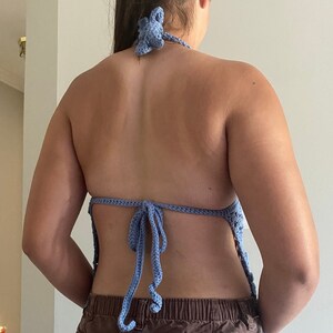 Pu&ograve; includere: Un top halter in crochet blu chiaro con lacci alla schiena. Il top &egrave; realizzato in un materiale morbido e leggero e ha un design delicato e femminile.