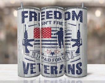 May include: A white tumbler with a wood grain pattern and a blue and red American flag design. The text "Freedom Isn't Free - Paid For It By Veterans" is printed on the tumbler.