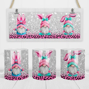 May include: Three white ceramic mugs with a pink and blue bunny gnome design. The gnomes are wearing pink bunny ears and hats with a white beard and blue clothing. The background is a silver glitter pattern with pink and black leopard print.