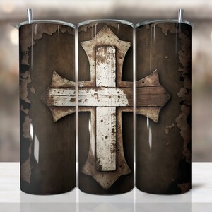 Könnte beinhalten: Drei Edelstahlbecher mit einem rustikalen Holzkreuzdesign. Das Kreuz ist weiß mit braunen Akzenten und auf einem braunen Hintergrund mit einem abgenutzten Look platziert.