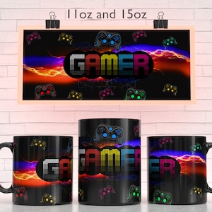 Puede incluir: Taza de café negra con temática de jugador. La taza presenta un texto "GAMER" pixelado de colores con rayos y mandos de videojuegos. Disponible en 11oz y 15oz.