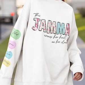 May include: White sweatshirt with the text "This Jamma wears her heart on her sleeve" in black with a floral design. The sleeves have colourful hearts with the words "Hold", "Your", "Own", and "Truth" on them.