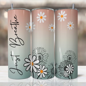May include: A stainless steel tumbler with a pink to green ombre design and a black and white daisy pattern. The tumbler has the text "Just Breathe" written on it in black cursive.