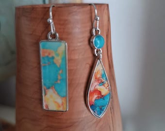 May include: A pair of silver earrings with turquoise, orange, and yellow stone inlays. One earring is rectangular, the other is teardrop-shaped. The earrings are displayed on a wooden stand.