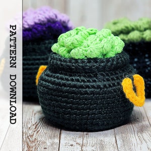 May include: Green crocheted cauldron with a yellow handle. The cauldron is filled with green yarn and is sitting on a wooden surface.