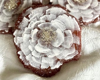 Puede incluir: Cuatro posavasos decorativos con diseño floral. Cada posavasos presenta una base roja oscura con detalles blancos en forma de pétalos y un centro brillante. Los posavasos están dispuestos sobre una superficie blanca texturizada.